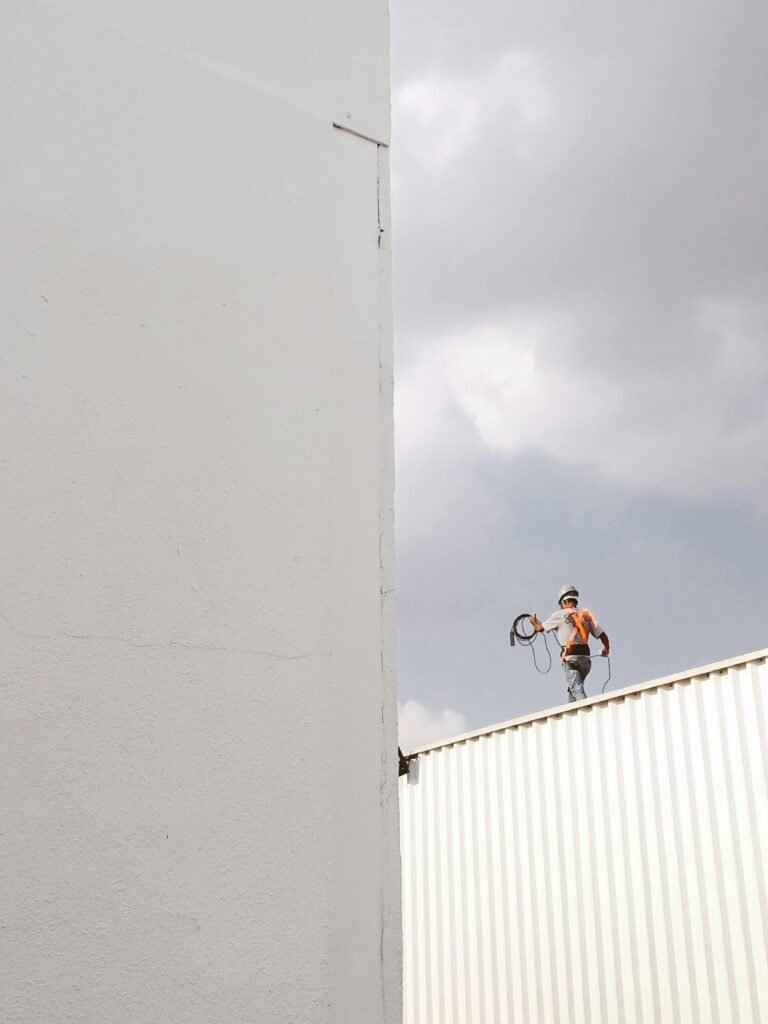 A construction worker stands on a rooftop against a large white wall, highlighting a minimalist aesthetic.